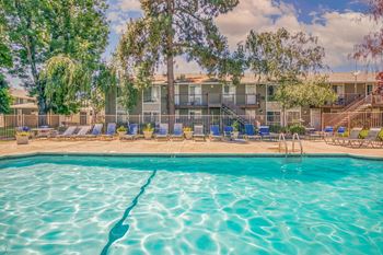 A swimming pool in front of a building with trees and chairs around it.
